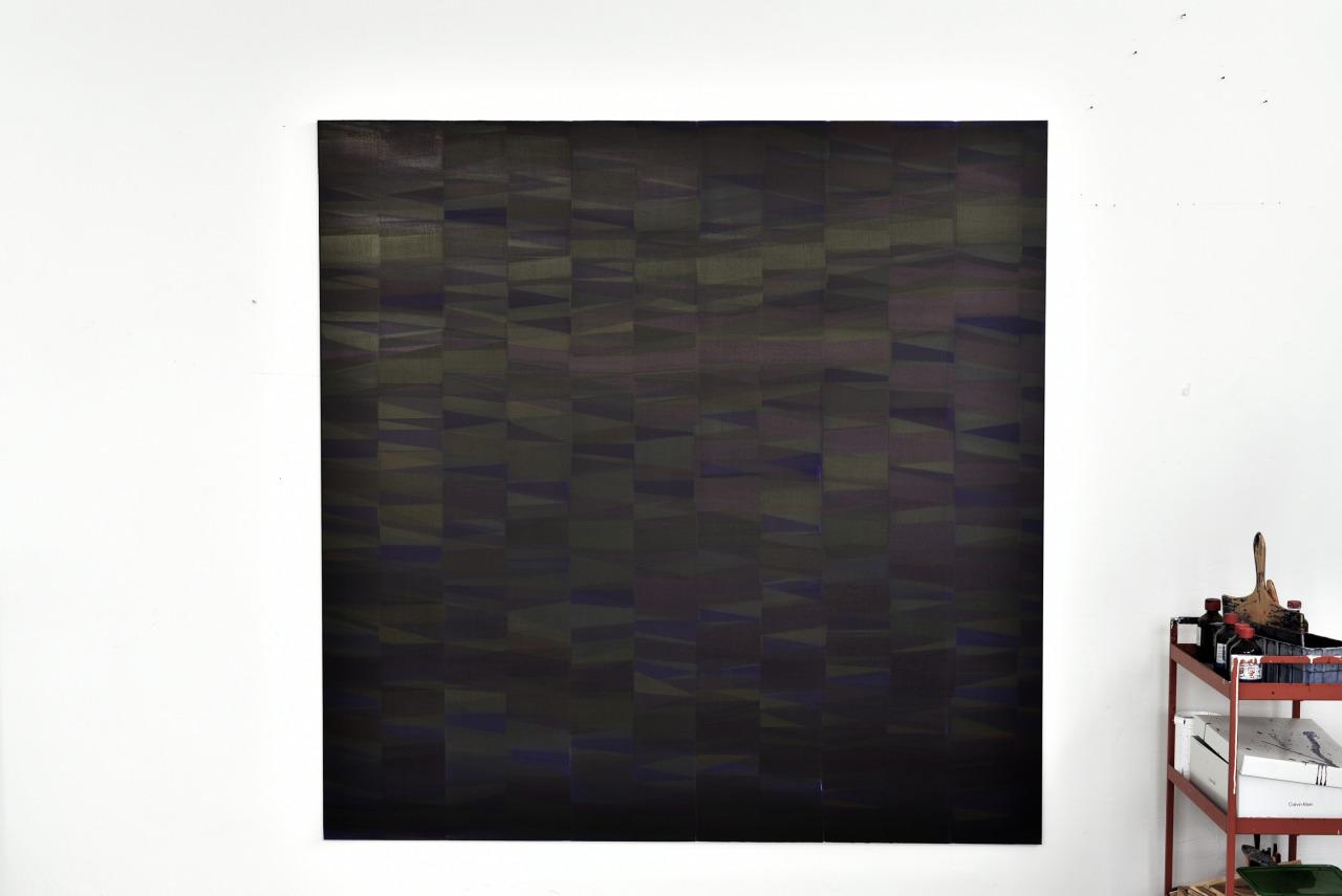 op180226. acrylic ink on canvas, 170 x 170 cm
This work is constructed through repeated, layered gestures applied in very thin, translucent passages of ink. The surface builds up slowly through overlapping geometric segments, where each layer slightly shifts in tone, direction, and density. Subtle variations accumulate, producing a muted, iridescent field that changes with light and viewing angle.
From a distance the painting appears restrained and nearly uniform, but at close range its internal structure begins to unfold into small displacements, rhythms, and optical tensions. The layered surface reacts sensitively to movement, making the work difficult to photograph accurately — much of its visual information exists between visibility and disappearance. Rather than depicting an image, the painting functions as a perceptual field shaped by repetition, duration, and instability.
